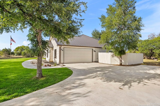 view of front facade featuring metal roof, an attached garage, fence, driveway, and a front lawn