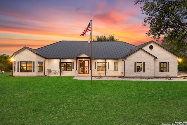 back of house at dusk with stone siding, a standing seam roof, and metal roof