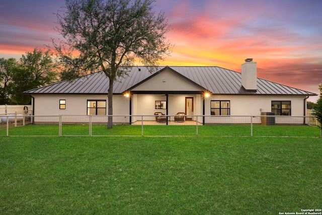 back of property at dusk featuring metal roof, fence private yard, a yard, stucco siding, and a standing seam roof