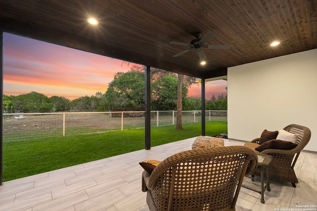 patio terrace at dusk featuring fence, a lawn, and ceiling fan