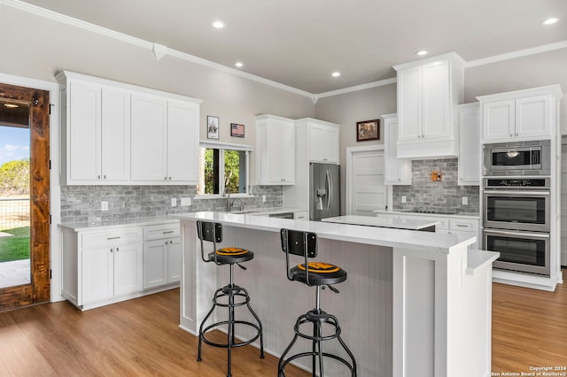 kitchen featuring a kitchen island, appliances with stainless steel finishes, a breakfast bar, light wood-style floors, and white cabinetry