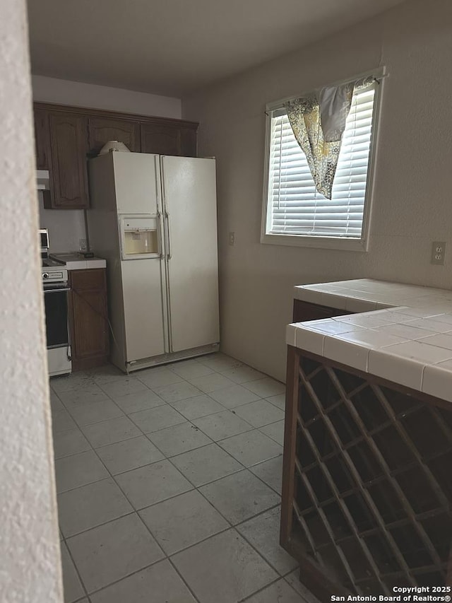 kitchen featuring tile counters, light tile patterned floors, gas range oven, and white fridge with ice dispenser