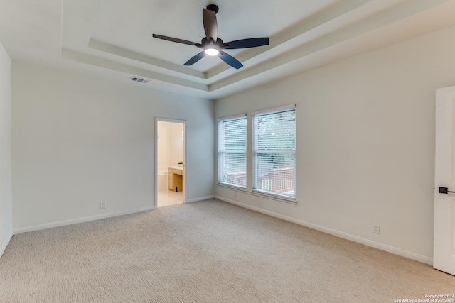 unfurnished bedroom featuring ceiling fan, light colored carpet, ensuite bathroom, and a raised ceiling