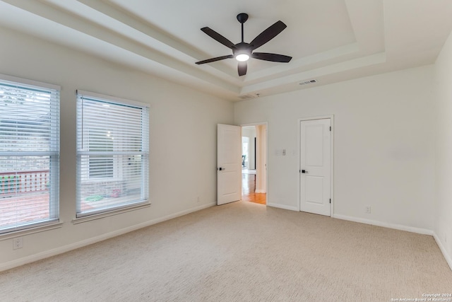 empty room featuring a raised ceiling, plenty of natural light, light colored carpet, and ceiling fan