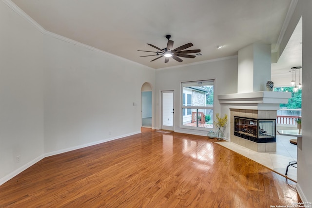 unfurnished living room featuring a tile fireplace, crown molding, ceiling fan, and light wood-type flooring