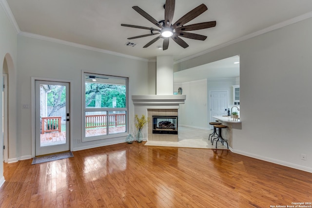 unfurnished living room featuring a tiled fireplace, ornamental molding, light hardwood / wood-style floors, and ceiling fan