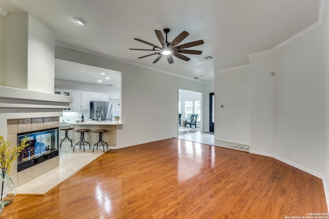 living room featuring crown molding, a tile fireplace, ceiling fan, and light wood-type flooring