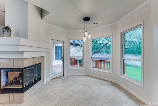 unfurnished dining area featuring crown molding, a tiled fireplace, and light tile patterned floors