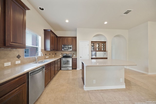 kitchen featuring appliances with stainless steel finishes, a kitchen island, decorative backsplash, sink, and light tile patterned floors