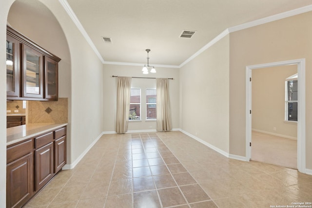 unfurnished dining area with light tile patterned floors, crown molding, and a chandelier