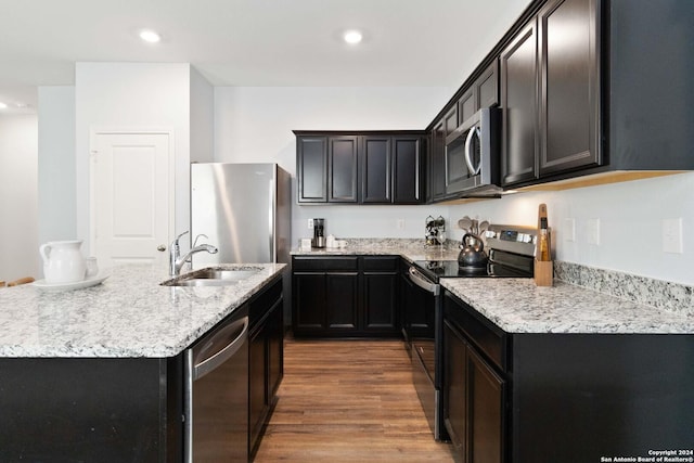 kitchen featuring recessed lighting, wood finished floors, appliances with stainless steel finishes, a sink, and light stone countertops