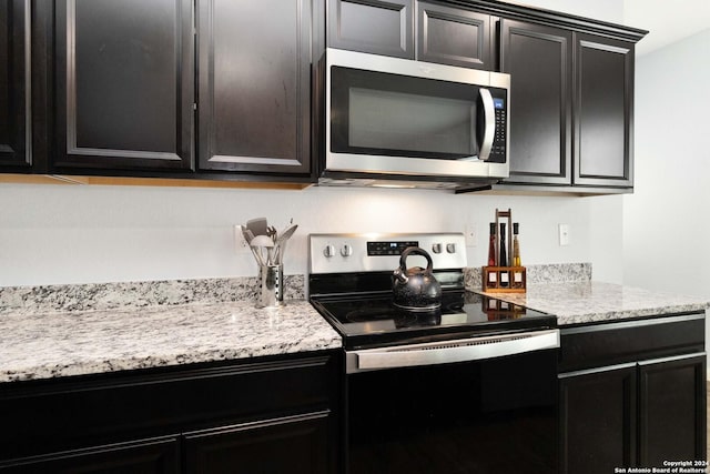 kitchen with appliances with stainless steel finishes, light stone counters, and dark cabinets