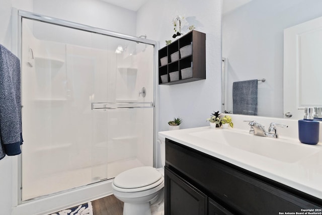 bathroom featuring wood finished floors, a shower stall, toilet, and vanity