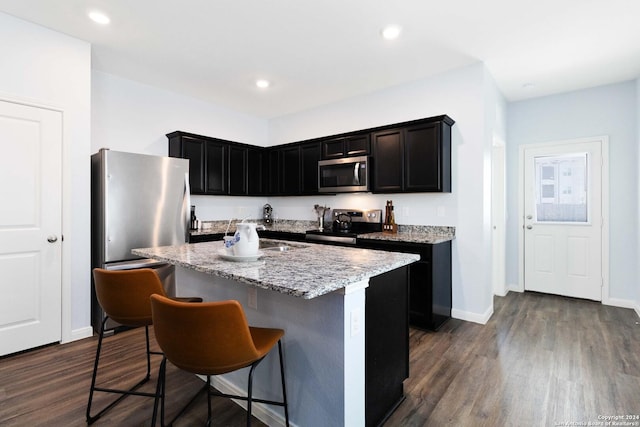 kitchen featuring a center island with sink, dark wood finished floors, a breakfast bar area, stainless steel appliances, and light stone countertops