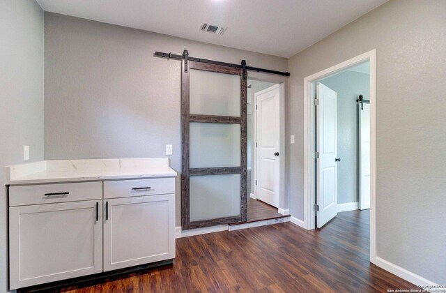 bar featuring white cabinetry, light stone countertops, dark hardwood / wood-style flooring, and a barn door