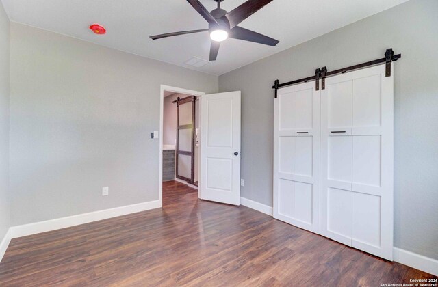 unfurnished bedroom with ceiling fan, hardwood / wood-style flooring, a barn door, and a closet