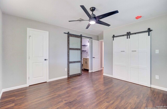 unfurnished bedroom featuring hardwood / wood-style floors, ensuite bath, ceiling fan, and a barn door