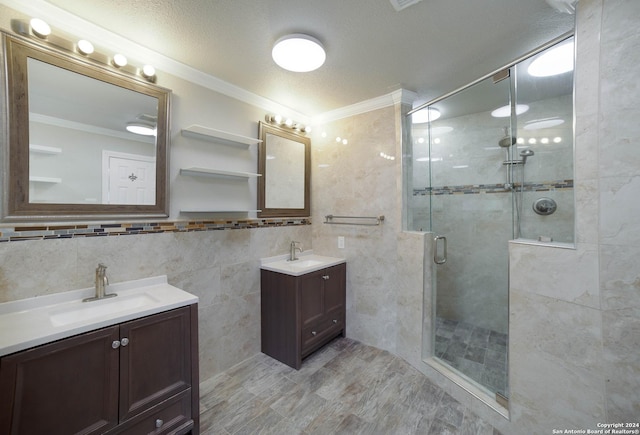 bathroom featuring crown molding, a sink, a stall shower, two vanities, and tile walls