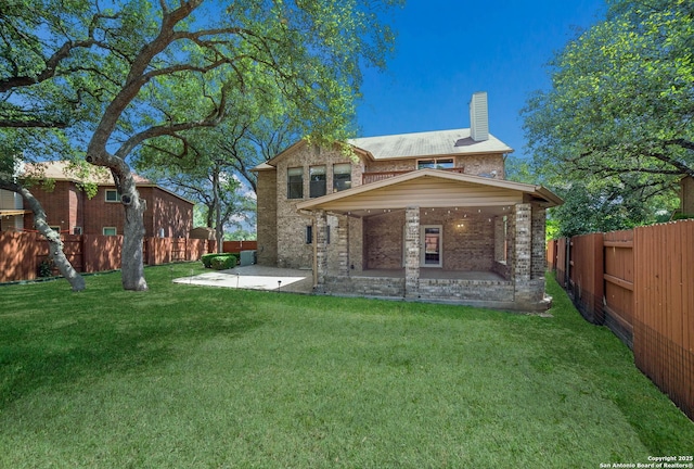 rear view of property with a chimney, a yard, brick siding, and a fenced backyard