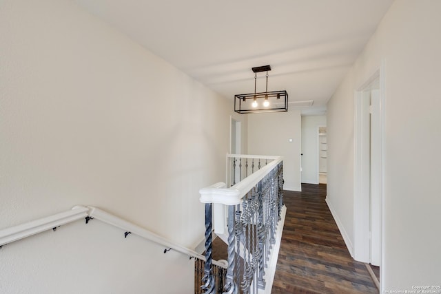 corridor featuring an upstairs landing, dark wood-type flooring, and baseboards