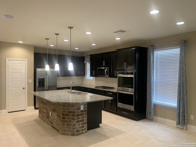 kitchen with sink, decorative light fixtures, an island with sink, stainless steel appliances, and light stone countertops