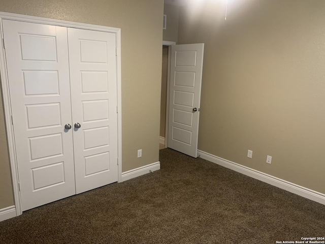 unfurnished bedroom with dark colored carpet and a closet