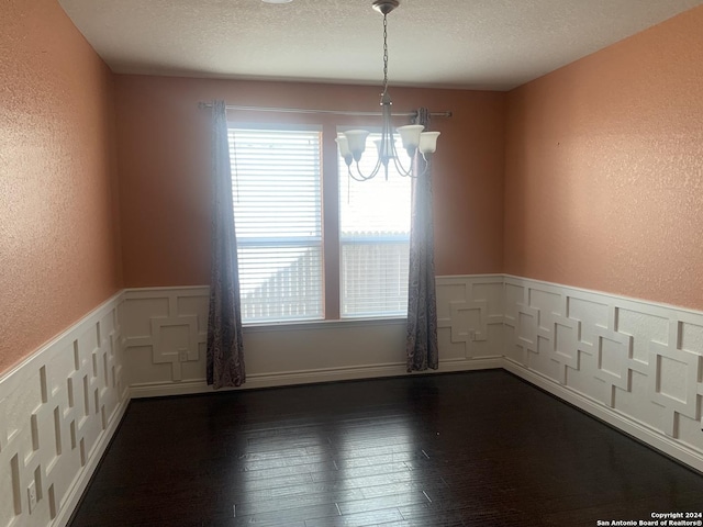 spare room featuring dark hardwood / wood-style flooring, a textured ceiling, and a chandelier