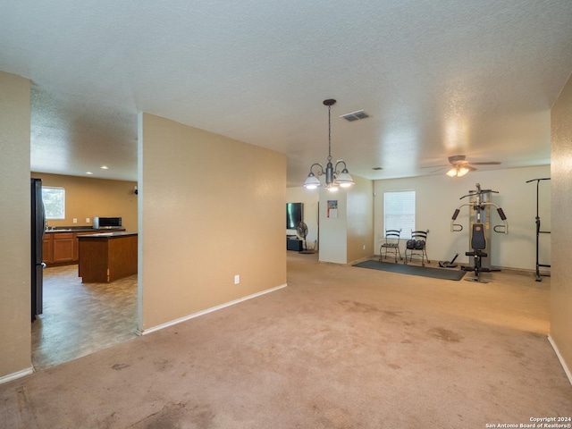 unfurnished living room featuring ceiling fan with notable chandelier and light carpet