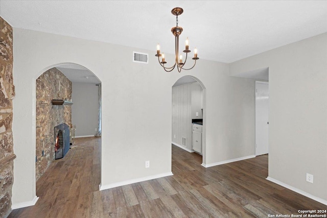 unfurnished dining area featuring dark wood-type flooring, a notable chandelier, and a fireplace