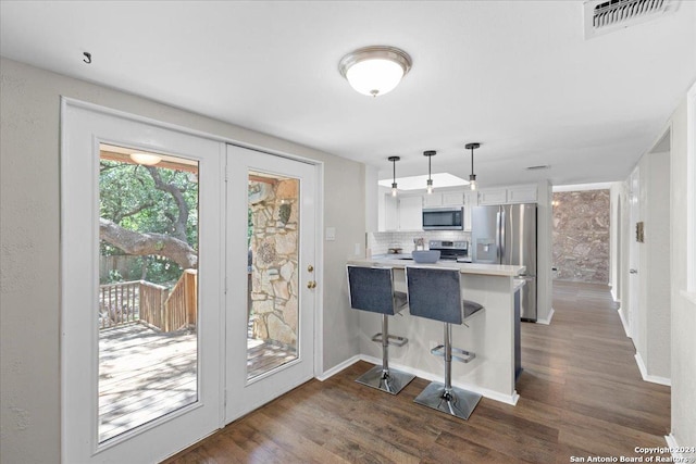 kitchen featuring appliances with stainless steel finishes, white cabinetry, hanging light fixtures, kitchen peninsula, and a breakfast bar area