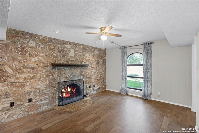 unfurnished living room with ceiling fan, dark wood-type flooring, a textured ceiling, and a stone fireplace