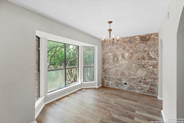 unfurnished dining area featuring a textured ceiling, an inviting chandelier, and hardwood / wood-style flooring