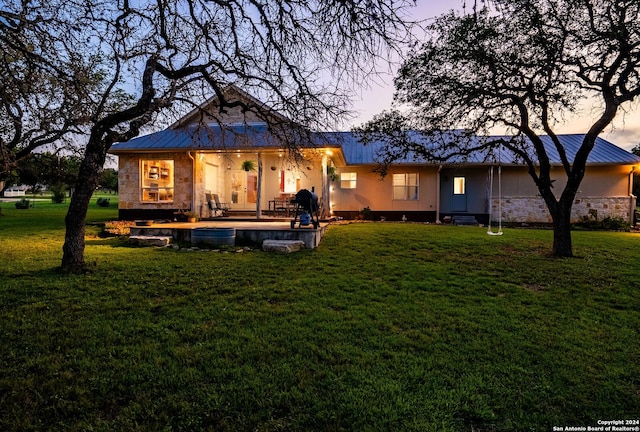 back of house with metal roof, stone siding, and a lawn