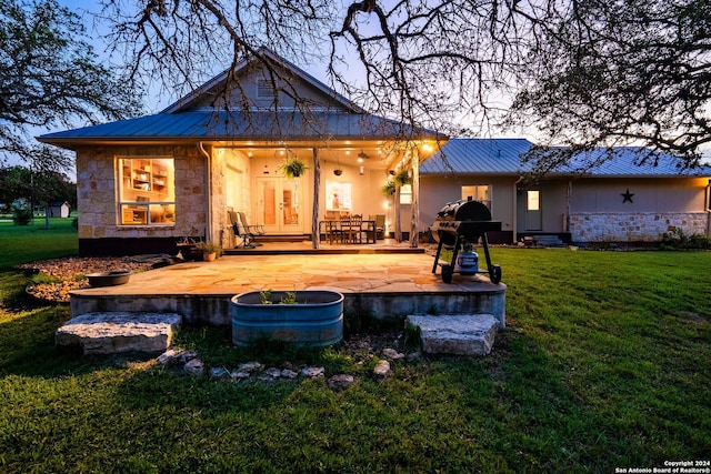 back of property with a yard, stone siding, a patio area, and metal roof