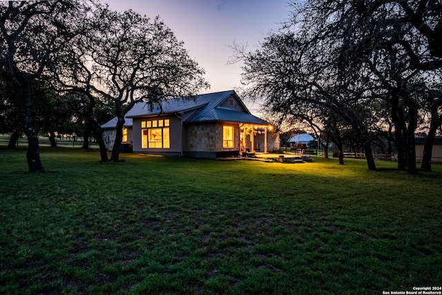 back of house at dusk featuring stone siding, a standing seam roof, metal roof, and a yard