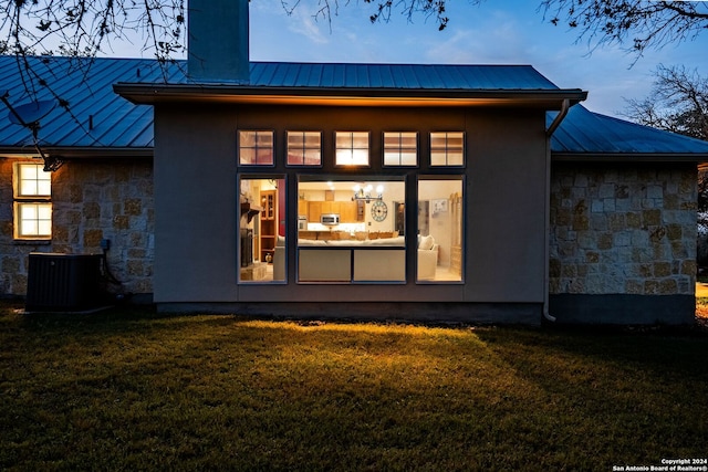 back house at dusk featuring a lawn and central AC unit