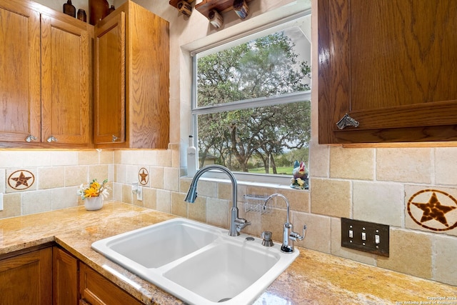 kitchen with brown cabinetry, light countertops, a sink, and backsplash