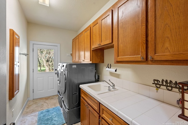 clothes washing area with sink, washing machine and dryer, cabinets, and light tile patterned floors