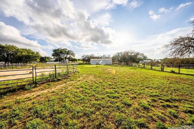 view of yard featuring a rural view, an outdoor structure, and fence