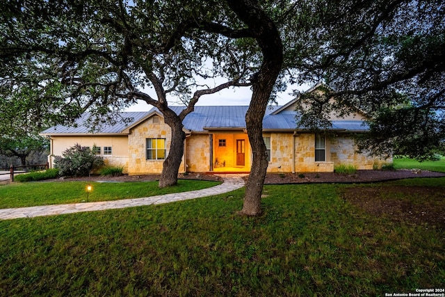 single story home with stone siding, a front yard, metal roof, and a standing seam roof