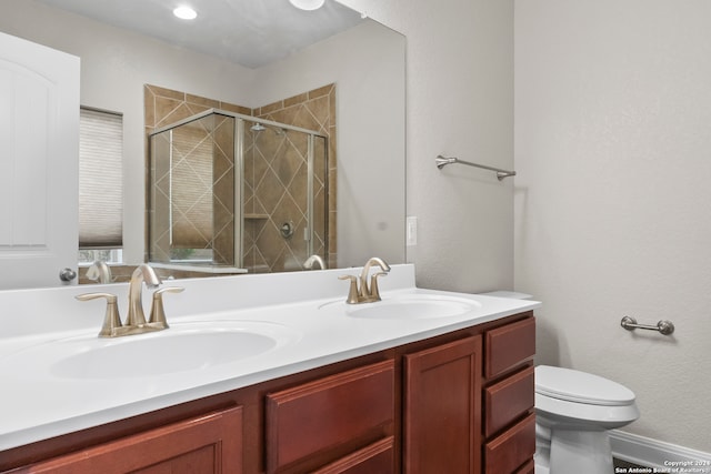 bathroom with a shower with shower door, double sink vanity, and toilet