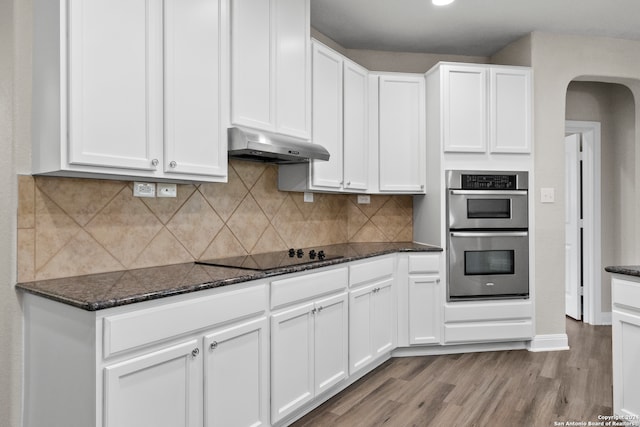 kitchen with light hardwood / wood-style flooring, dark stone counters, backsplash, white cabinetry, and stainless steel double oven