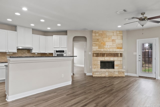 kitchen featuring white cabinets, a stone fireplace, hardwood / wood-style floors, and stainless steel oven