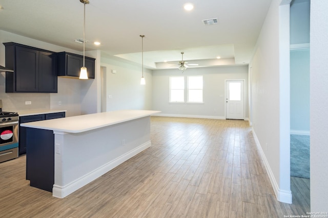 kitchen featuring stainless steel gas range oven, light hardwood / wood-style flooring, a center island, a raised ceiling, and ceiling fan