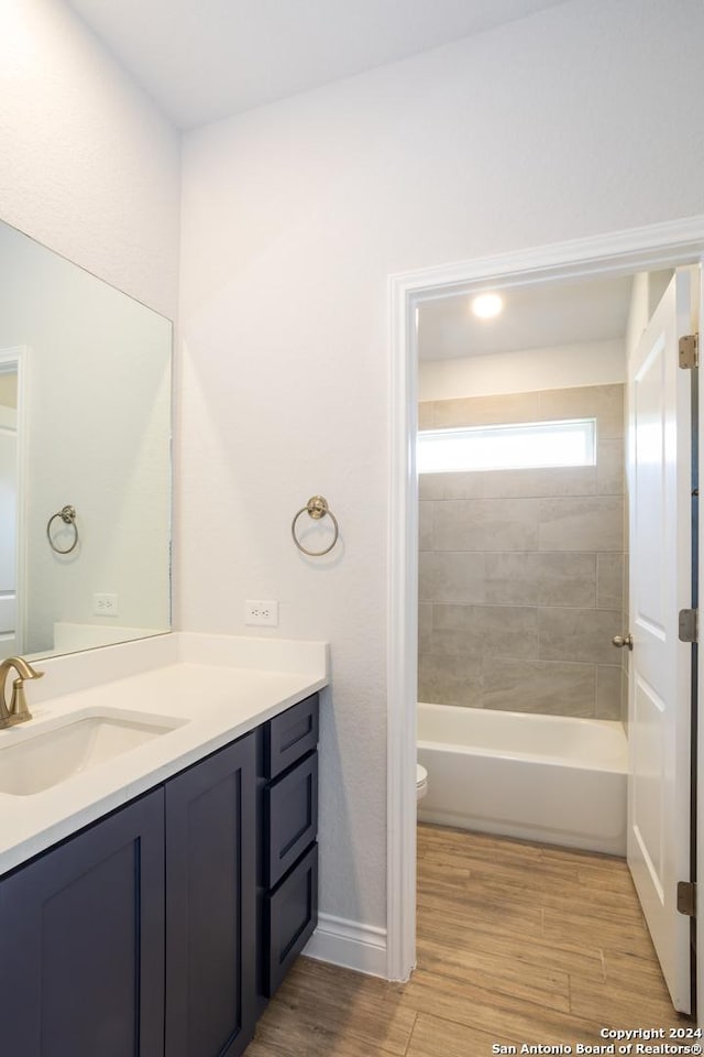 full bathroom with toilet, wood-type flooring, vanity, and tiled shower / bath combo