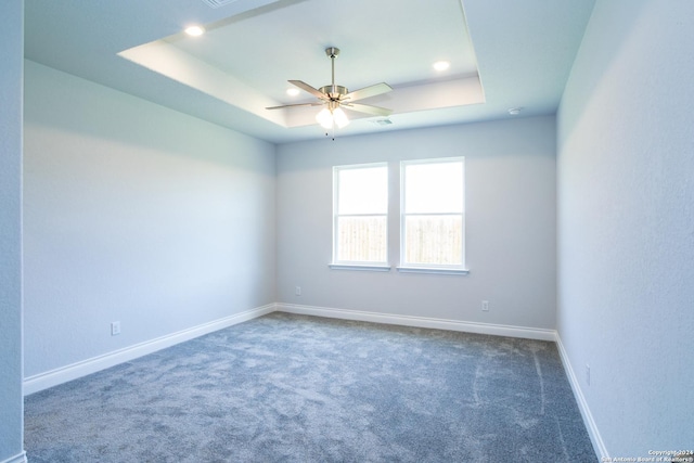 spare room featuring ceiling fan, dark colored carpet, and a tray ceiling