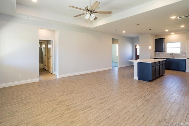 kitchen with sink, a center island, light wood-type flooring, hanging light fixtures, and a tray ceiling