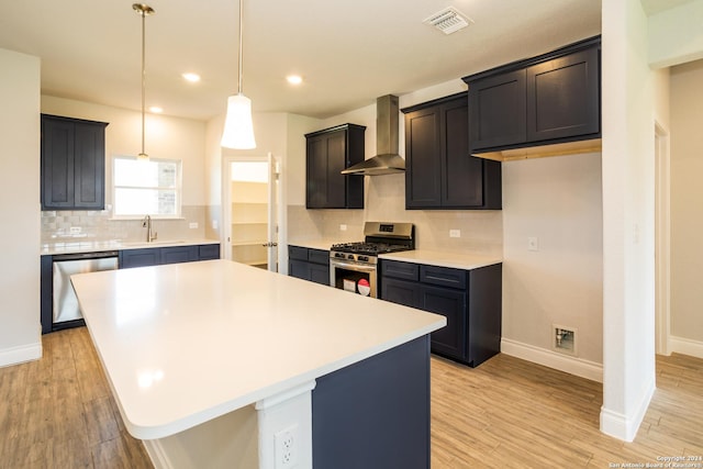 kitchen with appliances with stainless steel finishes, a center island, wall chimney exhaust hood, sink, and light hardwood / wood-style flooring