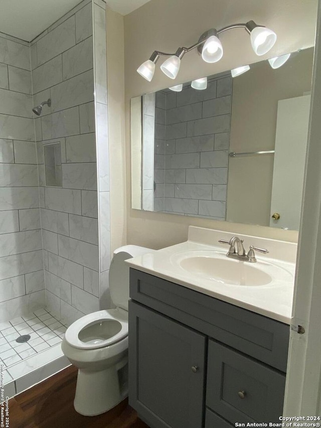 bathroom with toilet, hardwood / wood-style floors, tiled shower, and vanity