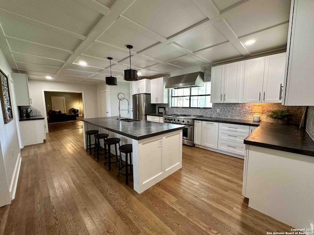 kitchen with white cabinets, dark countertops, appliances with stainless steel finishes, wall chimney range hood, and pendant lighting